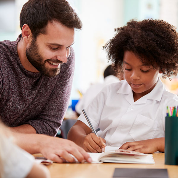 Male teacher with a student working in a notebook