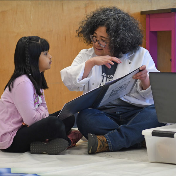 Teacher sitting on the floor cross-legged with a student